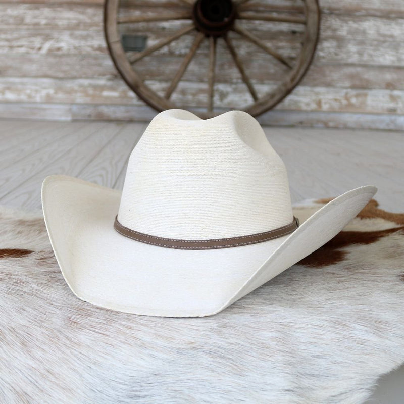 White straw cowboy hat with a brown band and upturned brim rests on a rustic wooden surface