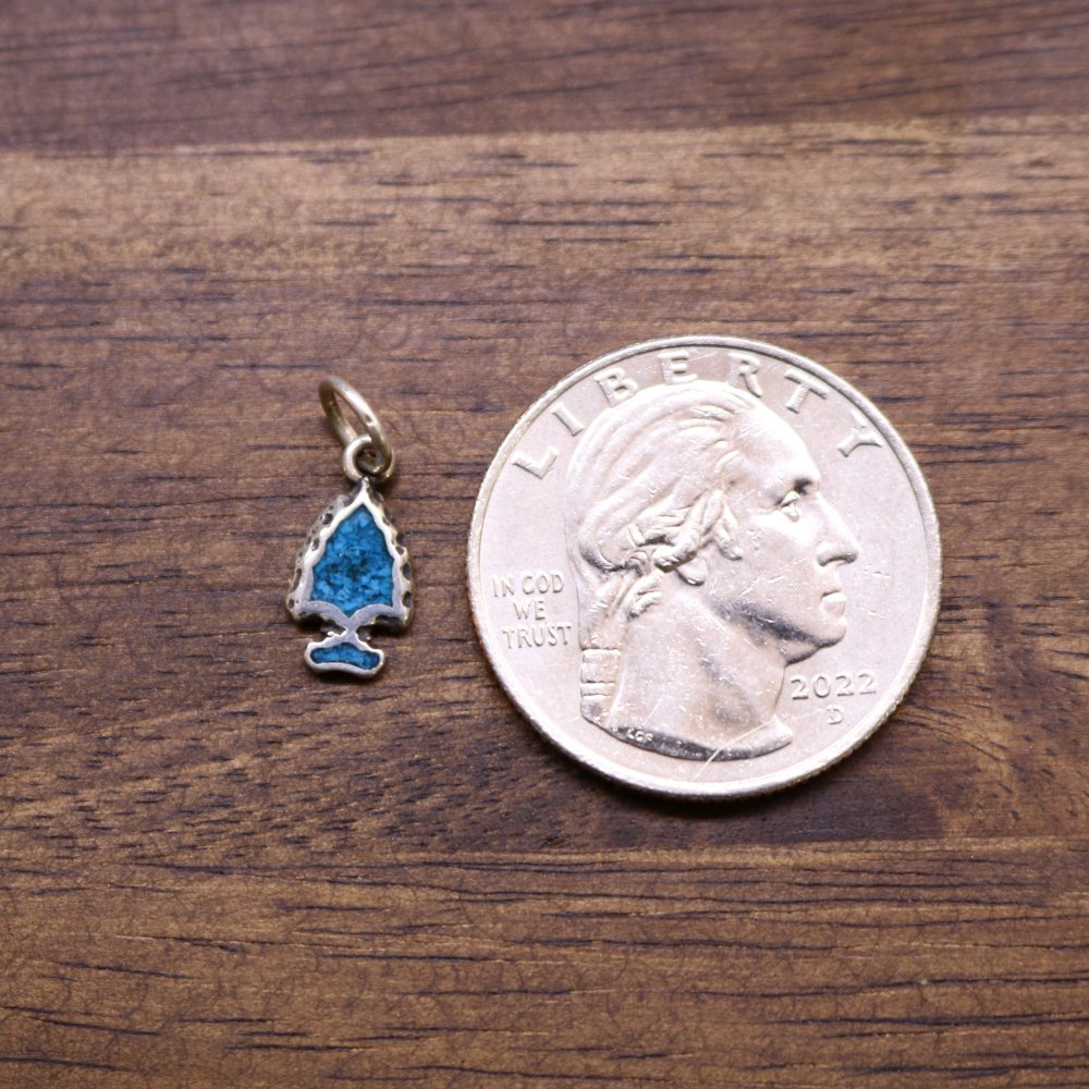 Turquoise inlay arrowhead charm next to a US quarter for size reference