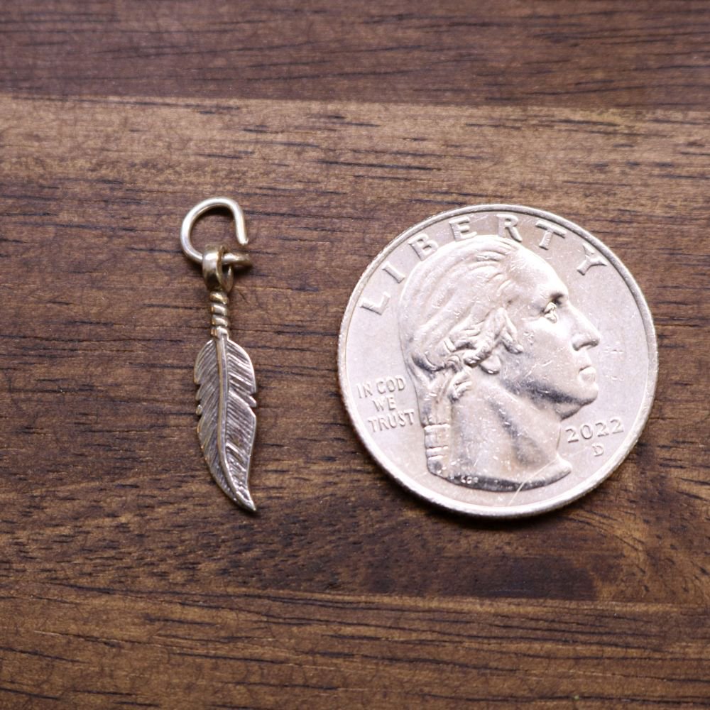 Sterling silver feather charm pendant beside a coin for size