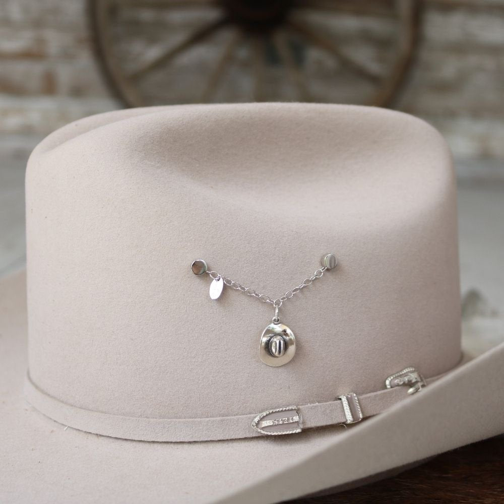 Sterling silver cowboy hat charm pendant hanging from chain on a beige cowboy hat.