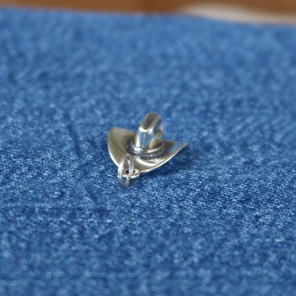 Sterling silver cowboy hat charm pendant with chain loop on blue fabric.