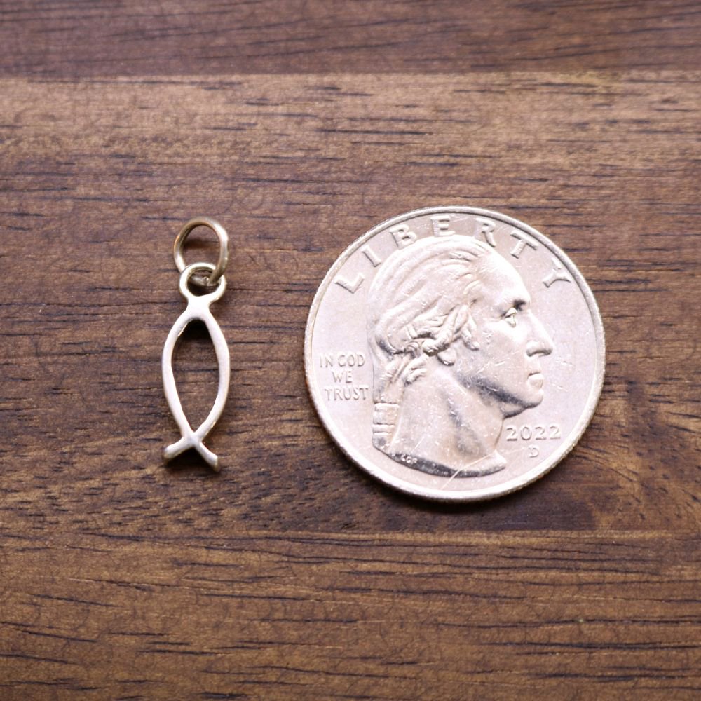 Sterling silver fish charm pendant next to a coin for size