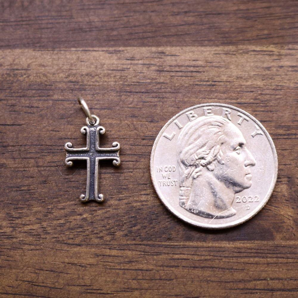 Sterling silver cross charm next to a coin for size, detailed ornate cross design