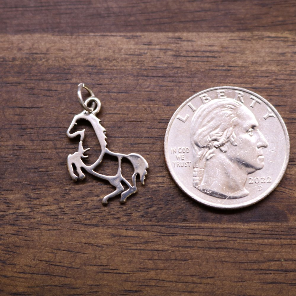Sterling silver rearing horse charm beside a coin for size comparison