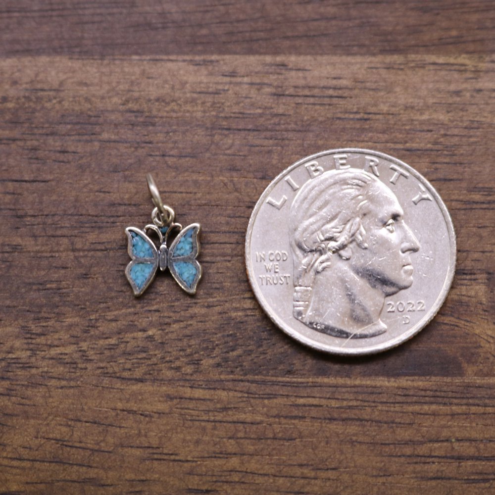 Sterling silver butterfly charm with blue enamel wings, shown alongside a coin for scale