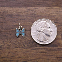 Sterling silver butterfly charm with blue enamel wings, shown alongside a coin for scale