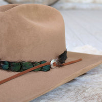 Sterling silver slotted concho on brown leather band with black and green feathers