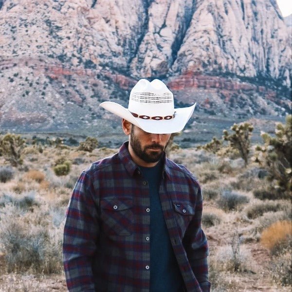 Cream straw cowboy hat with brown band, perforated crown and curved brim
