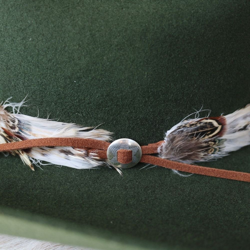 Silver slotted concho centered on brown leather band with feathers
