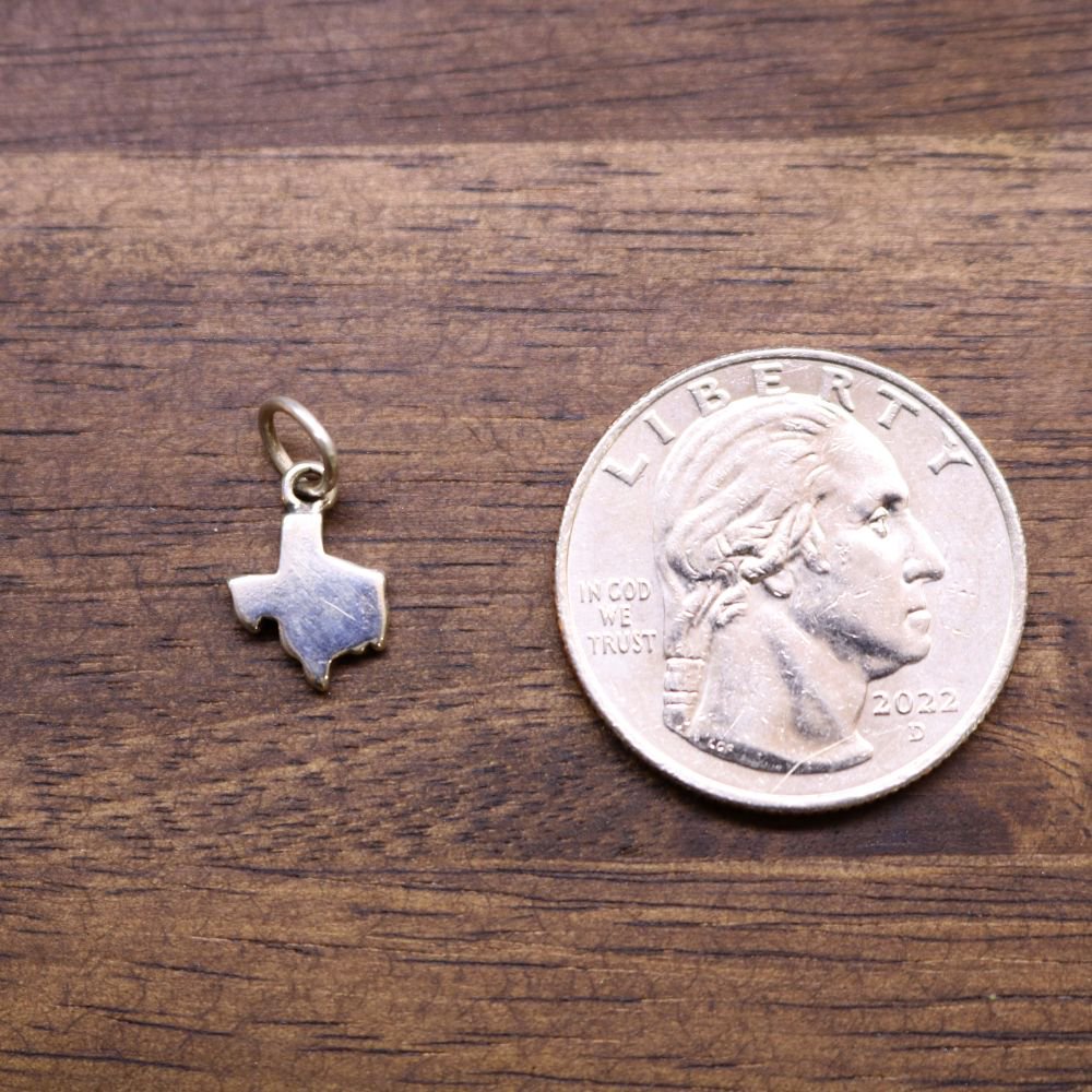 Sterling silver Texas-shaped charm next to a coin for size