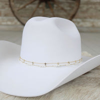 Gold-plated cross hat band chain with small charms on a white cowboy hat