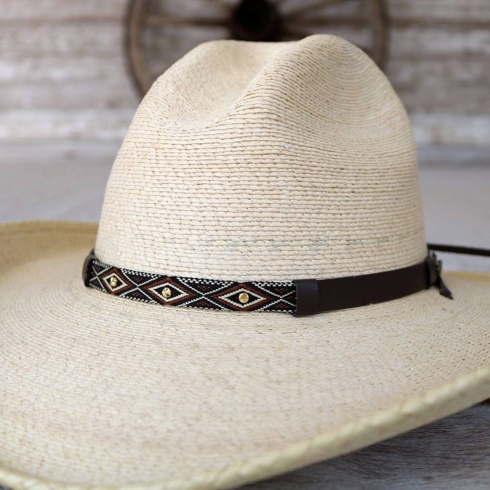 Cream palm leaf straw cowboy hat with dark belt-style band and geometric trim.
