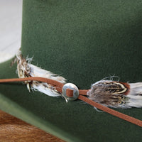 Silver slotted concho on brown leather band with feather ends